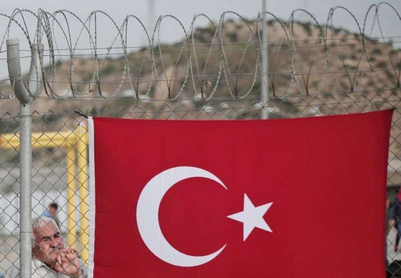 A migrant man stands behind a fence, decorated with a Turkish flag at the Nizip refugee camp in Gaziantep province, southeastern Turkey on April 23. (Lefteris Pitarakis/Associated Press)