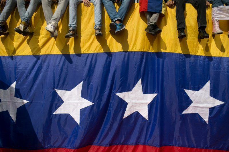 Un grupo de venezolanos se sienta sobre una bandera para protestar contra el presidente Nicolás Maduro en Caracas, Venezuela. Credit Alejandro Cegarra/Associated Press