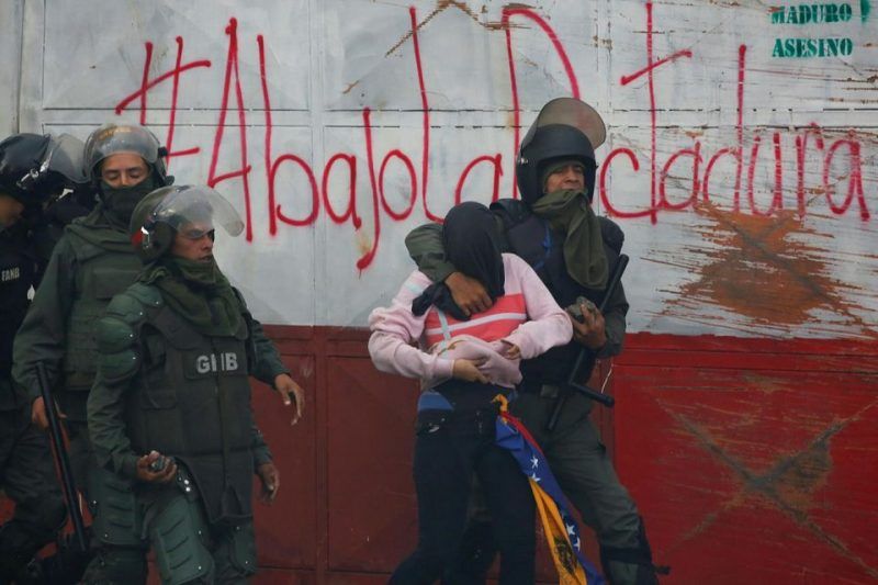 Un manifestant retenu par des policiers ­antiémeute à Caracas, le 28 juillet. Sur le mur est inscrit : «A bas la dictature.» Photo Carlos Garcia. Reuters.