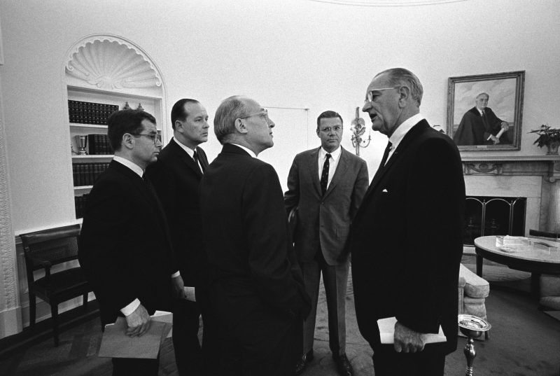 Walt Rostow, third from left, speaking to Lyndon Johnson in the Oval Office in 1967. Between them, in the background, is Robert McNamara. Credit LBJ Presidential Library