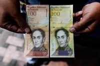 A man holds the new 100,000-bolivar note, right, to demonstrate its resemblance to the 100 note, in Caracas on Nov. 9. The new bill is worth about $30 on the official market and $2 on the black market. (Federico Parra/AFP)