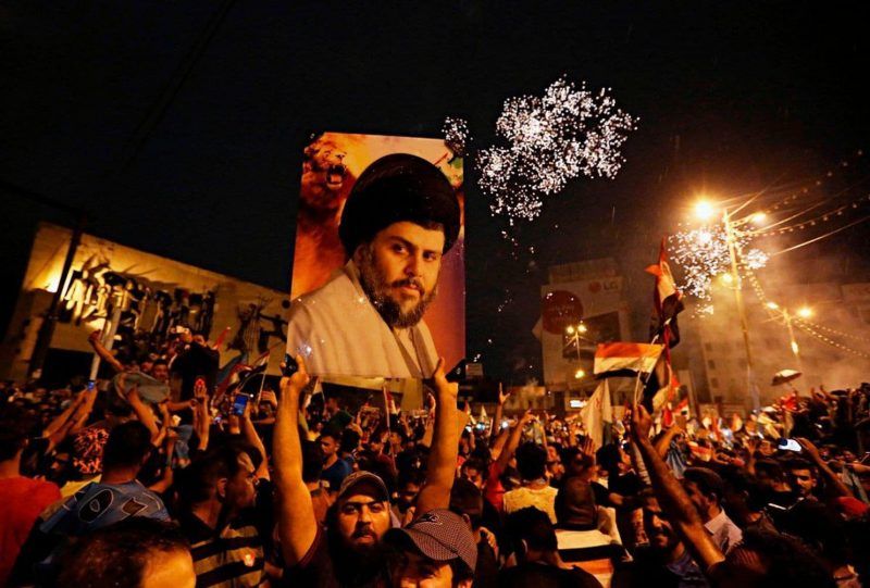In this May 14 photo, supporters of Shiite cleric Muqtada al-Sadr carry his image as they celebrate in Baghdad’s Tahrir Square. (Hadi Mizban/Associated Press)