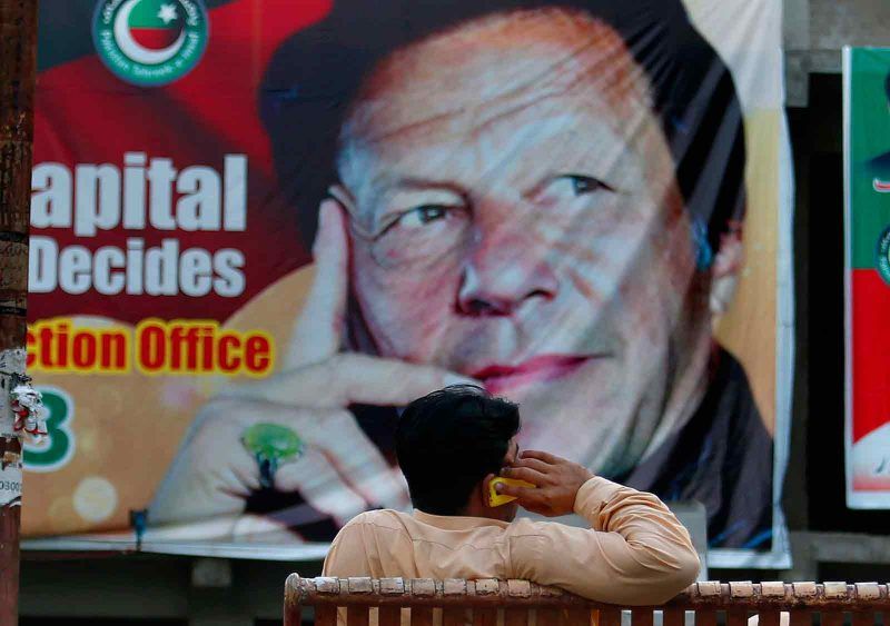 Anjum Naveed/AP Images A man on his cell phone sitting in front of a poster showing Imran Khan, head of the Pakistan Tehreek-e-Insaf party, which won last week’s elections, Islamabad, Pakistan, July 28, 2018