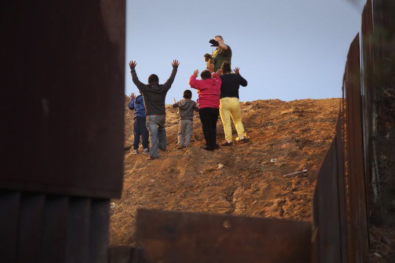 Un grupo de migrantes, miembros de la caravana que aguarda en un refugio en Tijuana, se entregó a un agente fronterizo el 3 de diciembre de 2018, en la frontera entre Tijuana y San Diego. Credit John Moore/Getty Images