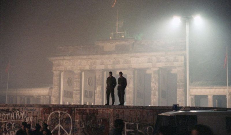 FILE - In this Nov. 14, 1989 file photo two East German border guards patrolled atop of Berlin Wall with the illuminated Brandenburg Gate in background, in Berlin. (AP Photo/Jockel Finck, file)