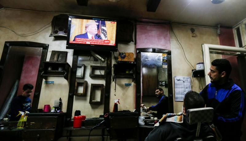 Palestinians watch the televised press conference of Donald Trump and Benjamin Netanyahu on 28 January 2020 at a barber shop in Gaza City. Photo: Getty Images. 