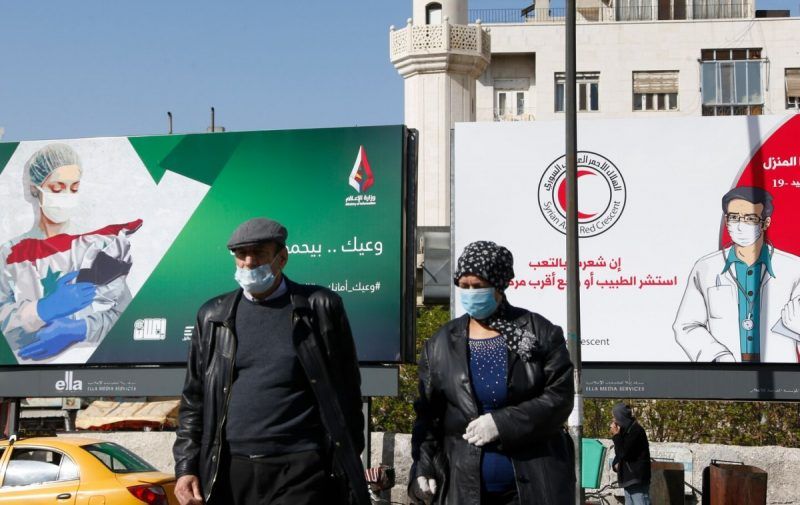 Syrians wearing face masks walk past billboards with messages about the coronavirus in Damascus on April 1. (Louai Beshara/AFP via Getty Images)