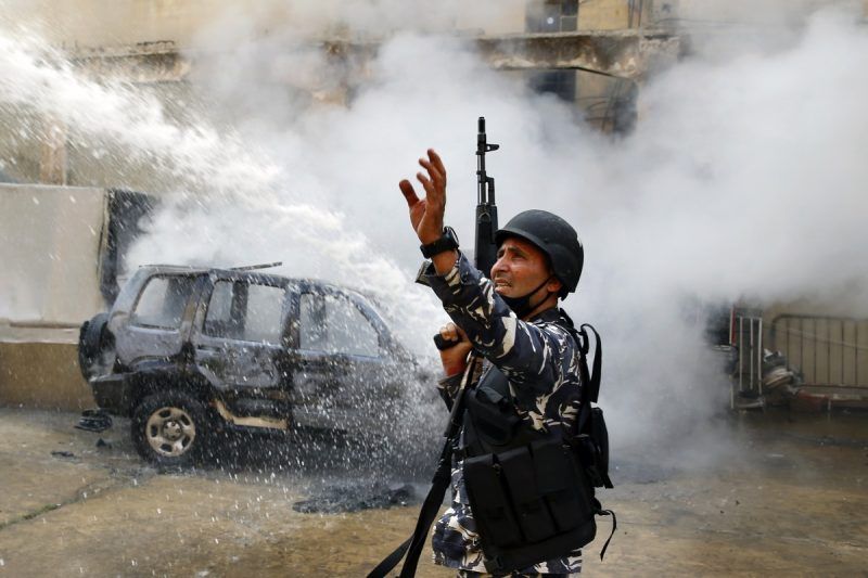 A police officer gestures to firefighters as they extinguish a police car that was set on fire by antigovernment protesters in Tripoli, Lebanon, on April 28. (Bilal Hussein/AP)