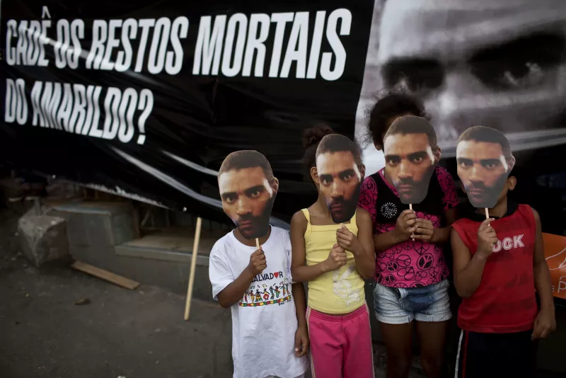 Children cover their faces with photos of Amarildo de Souza next to a banner reading “Where are Amarildo’s mortal remains?” at a protest in Rio de Janeiro in 2013. Credit Felipe Dana/Associated Press