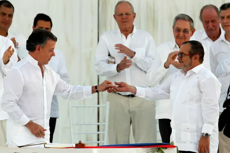 Colombian President Juan Manuel Santos, left, hands a lapel pin in shape of a dove to Marxist rebel leader Rodrigo Londoño (‘Timochenko’) after signing the accords ending a half-century war in 2016 © John Vizcaino/Reuters
