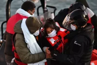 A member of the British Border forces and another man help a child to disembark from a boat with other migrants, in Dover, England, on April 18. (Ben Stansall/AFP via Getty Images)