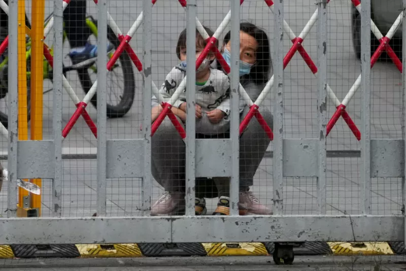 A masked woman and a child look out through the barrier at a closed residential area during lockdown to contain spread of the coronavirus in Shanghai on May 10. (Aly Song/Reuters)
