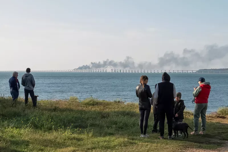 People watching smoke rising from damaged sections of the bridge over the Kerch Strait, Crimea, October 2022. Stringer / Reuters